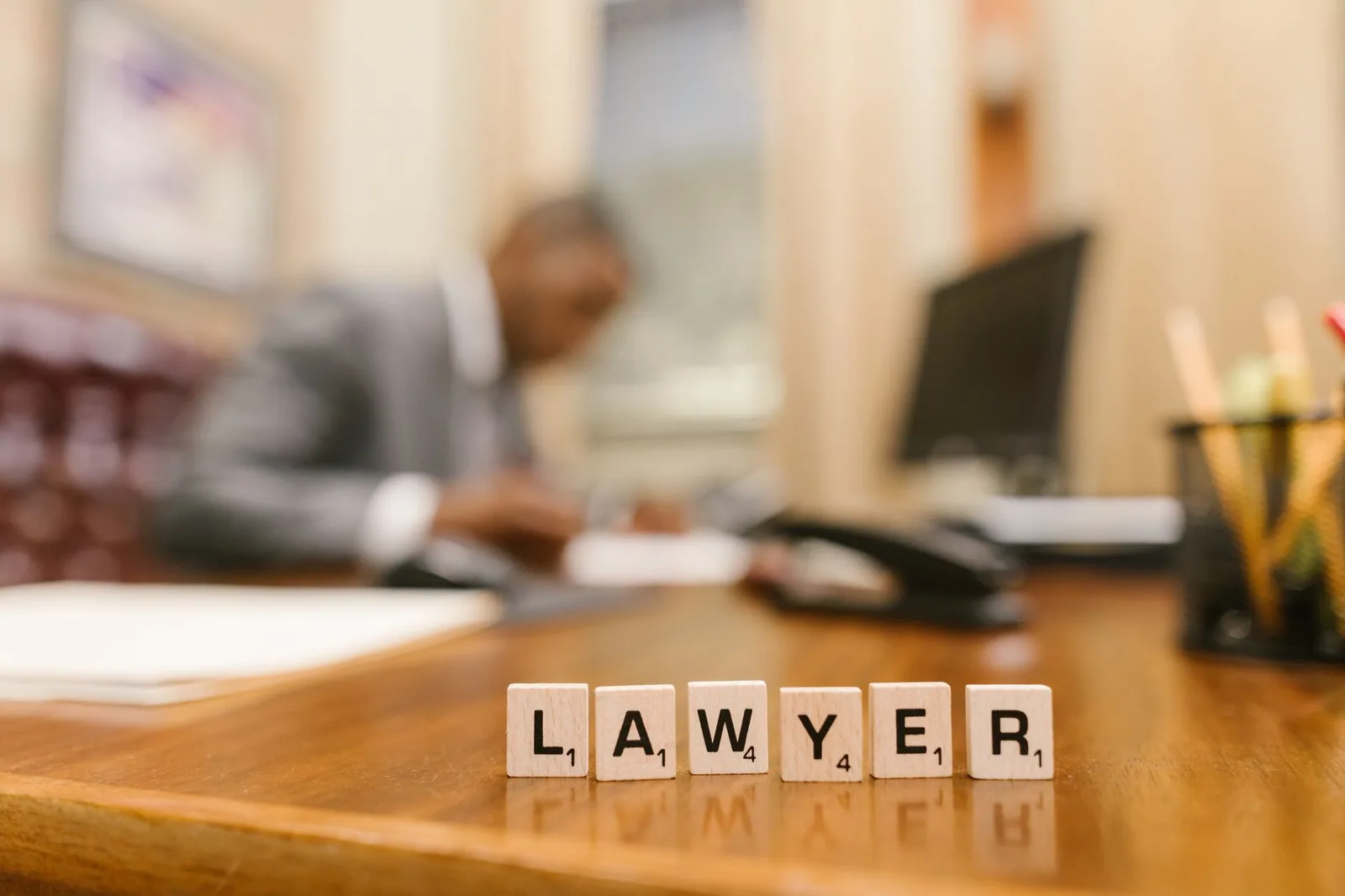 Letras de madeira formando a palavra 'LAWYER' em uma mesa, com um escritório desfocado ao fundo, ilustrando benefícios de