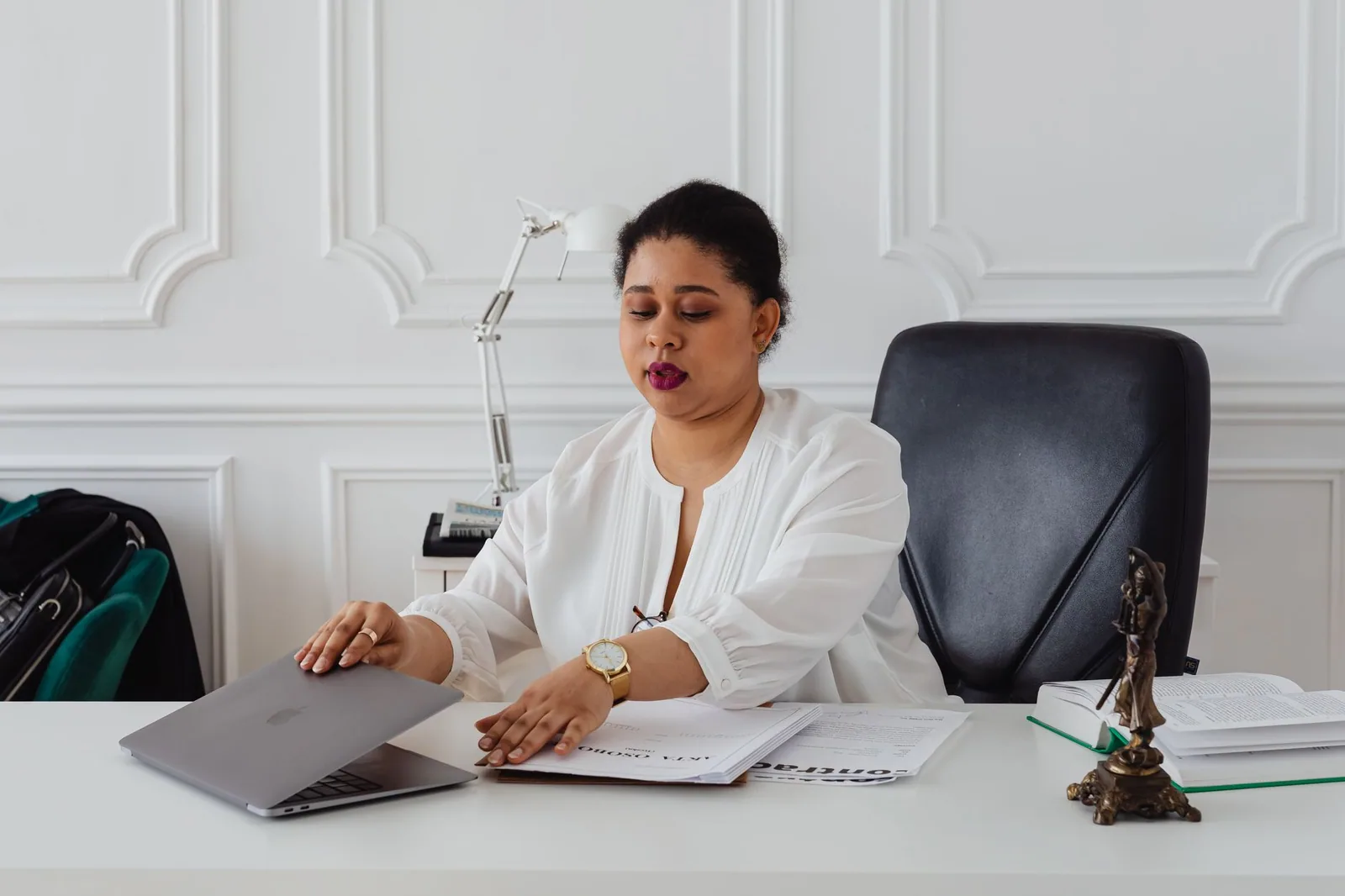 Mulher confiante de blusa branca em escritório moderno, com laptop e documentos jurídicos, representando marketing digital